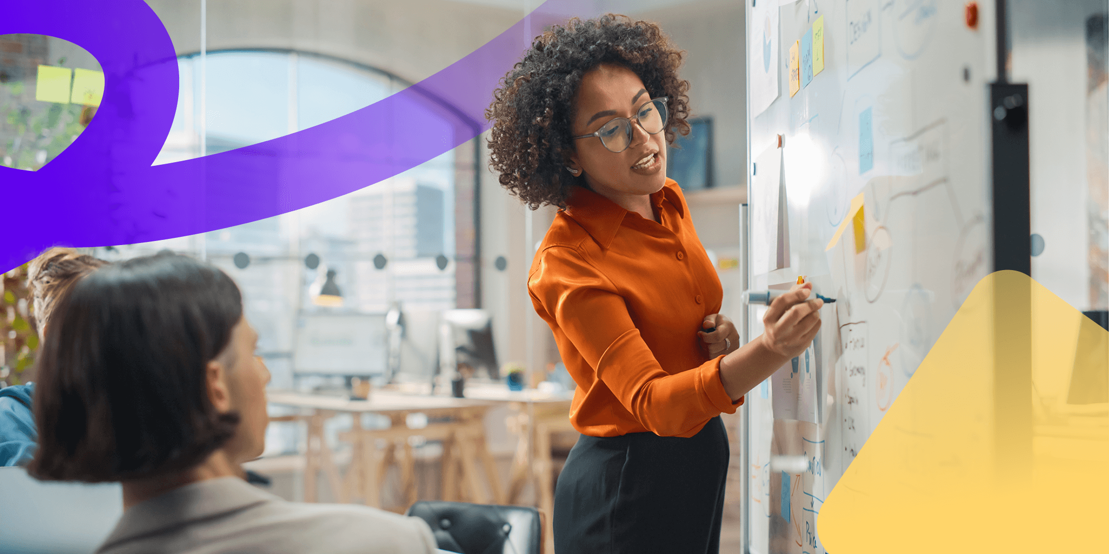 A woman is standing up and writing on a whiteboard to show her colleagues how to create an internal comms channel matrix.